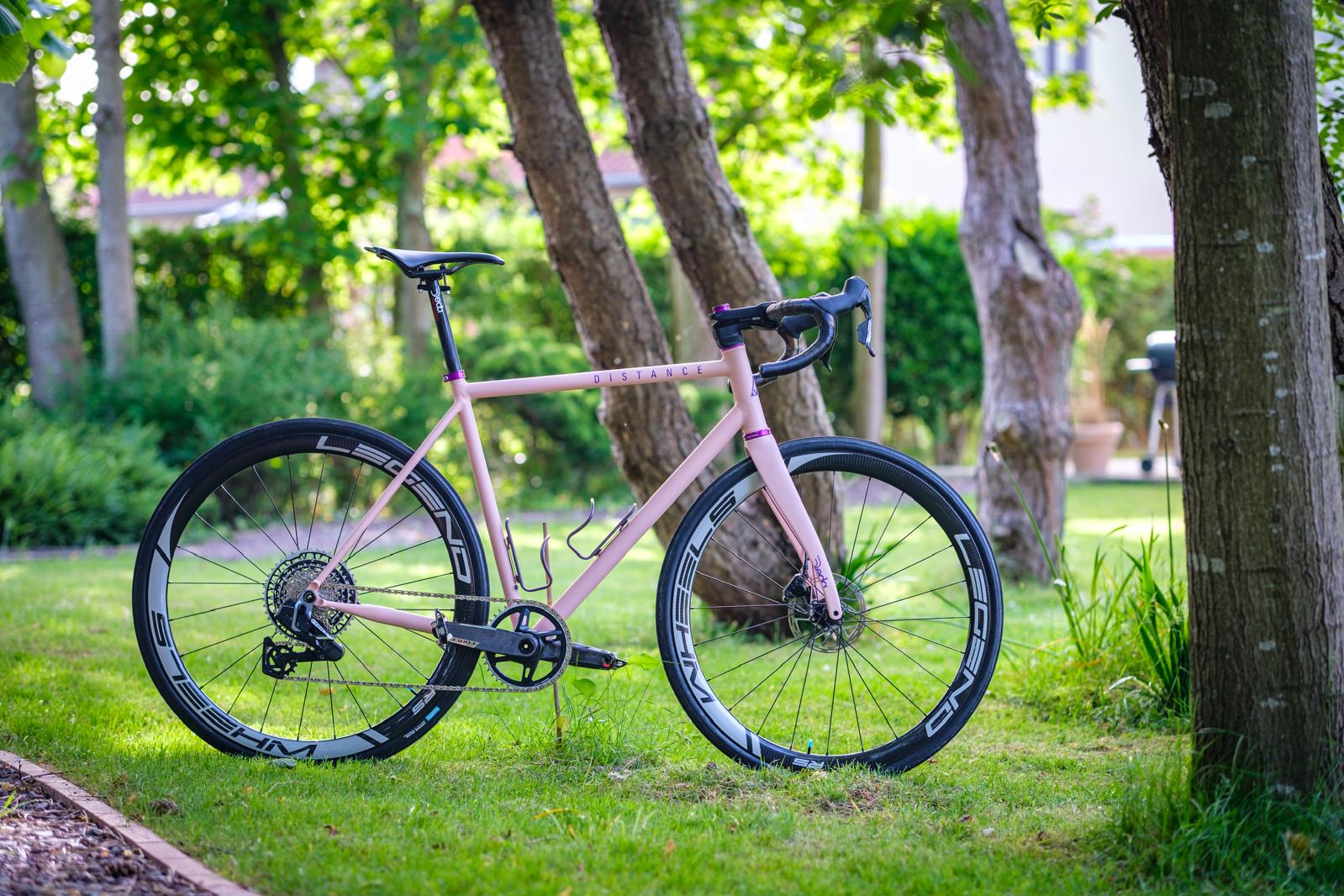 Distance 40i rose coquille mat de profil dans un jardin, roues carbone Legend